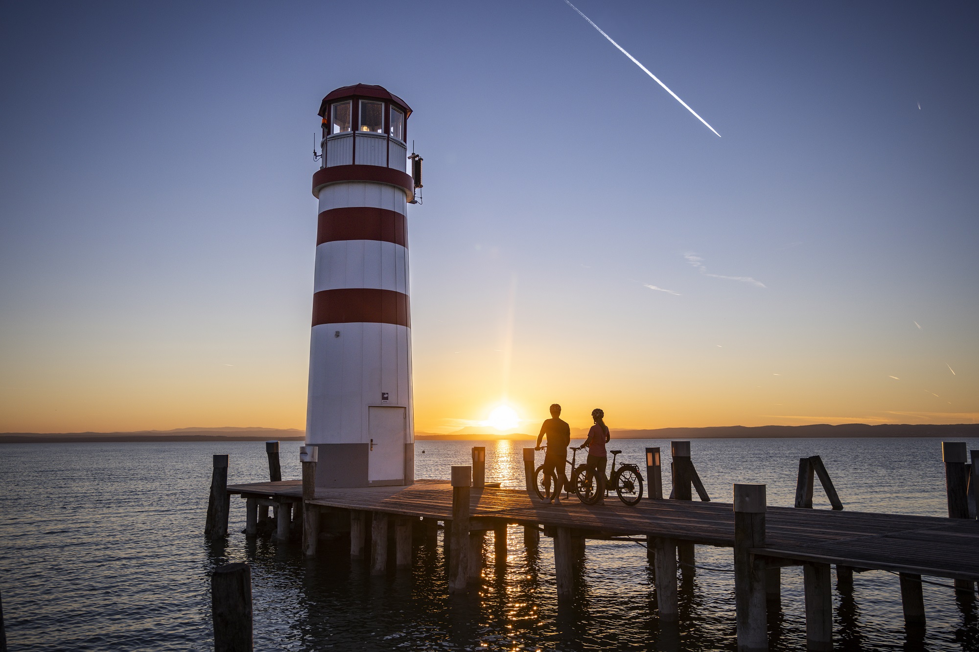 fietsers op een steiger bij een rood-witte vuurtoren