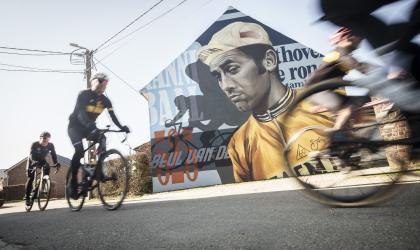 Wielrenners fietsen langs een muurschildering op de Eddy Merckx fietsroute